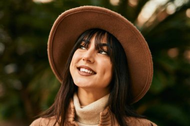 Parkta gülümseyen, kışlık şapkalı esmer kadın.