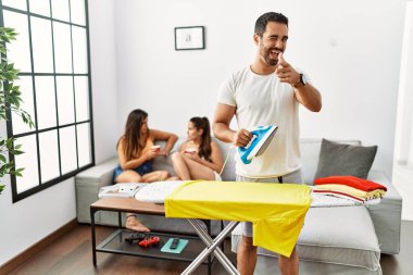 Genç İspanyol adam evde kıyafetlerini ütülüyor ve mutlu ve komik yüzüyle kamerayı işaret ediyor. iyi enerji ve titreşimler. 