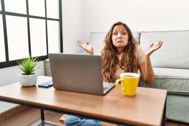 Güzel İspanyol kadın evinde bilgisayar kullanıyor. Hiçbir şeyden haberi yok ve elleri ve kolları havada. şüphe kavramı. 