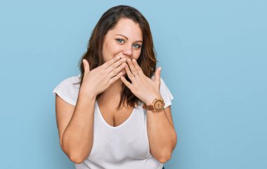 Genç ve cüsseli bir kadın, günlük beyaz tişört giyip gülüyor ve utanıyor kıkırdıyor ağzı ellerle, dedikoduyla ve skandal konseptiyle örtüyor. 