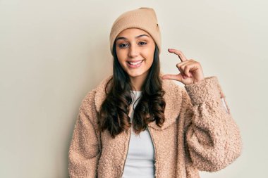 Yün kazak giyen, kışlık şapkalı, gülümseyen, kendine güvenen, el hareketi yapan, parmaklarıyla işaret yapan ve kameraya bakan genç İspanyol kadın. ölçüm kavramı. 