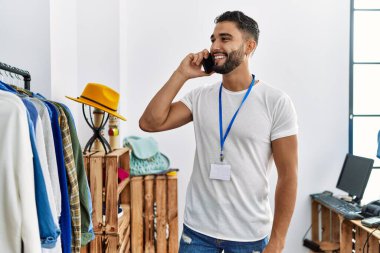 Genç Arap esnaf akıllı telefondan konuşuyor giyim mağazasında elbise rafının yanında duruyor.