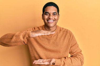 Genç, yakışıklı, sıradan bir süveter giyen, elleri büyük ve büyük bir işaret gösteren, ölçü sembolü olan bir İspanyol. Kameraya bakıp gülümsüyor. ölçüm kavramı. 