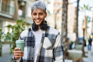Genç İspanyol adam şehirde kahve içerken kulaklık takıyor..