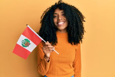 Afro saçlı, elinde Peru bayrağı olan Afro-Amerikan bir kadın. Olumlu ve mutlu görünüyor. Kendine güvenen bir gülümsemeyle dişlerini gösteriyor. 