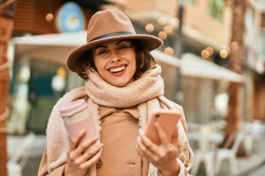 Genç İspanyol kadın akıllı telefon kullanıyor ve şehirde kahve içiyor..