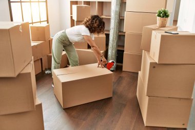 Orta yaşlı İspanyol kadın yeni evinde karton kutu paketlerken kendine güler.