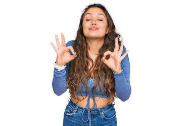 Gündelik kıyafetler giyen, gözleri kapalı gülümseyen genç İspanyol kız parmaklarıyla meditasyon hareketi yapıyor. yoga konsepti. 