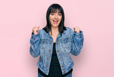 Gündelik giysiler giyen genç İspanyol kadın şaşkınlık ve şaşkınlık içinde kollarını kaldırarak ve gözlerini açarak başarıyı kutluyor. Kazanan konsept. 