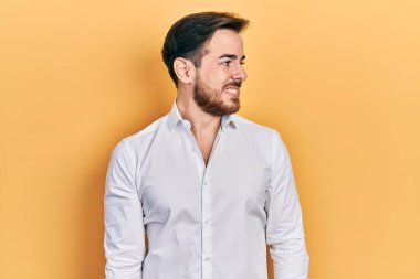 Sakallı, beyaz iş gömleği giyen yakışıklı beyaz bir adam. Taraf arıyor, rahat bir görünüm takınıyor. Kendine güvenen bir gülümsemesi var.. 