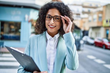 Profesyonel giyinen genç İspanyol iş kadını şehrin işçi panosuna gülümsüyor.