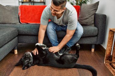 Genç İspanyol gülümseyen adam evde köpekle oynarken mutlu oluyor..