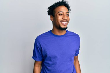 Sakallı, günlük mavi tişörtlü, rahat profil pozu veren, doğal yüzlü ve kendinden emin gülümseyen Afro-Amerikan genç adam.. 