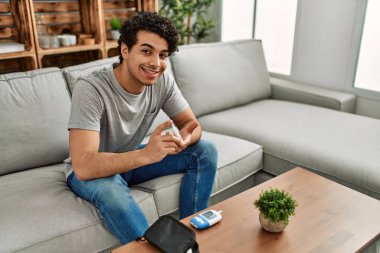 Evdeki kanepede oturan ve glikoz ölçen genç İspanyol diyabetik adam..