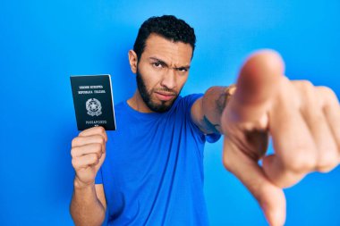 İtalyan sakallı, elinde pasaport olan İspanyol bir adam kameraya kızgın ve sinirli bir şekilde bakıyor. 