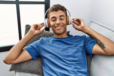 Genç İspanyol adam evde kulaklık takarak kanepede rahatlıyor.