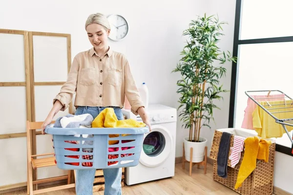 年轻的高加索女人微笑着 自信地拿着篮子和衣服在洗衣房里 — 图库照片