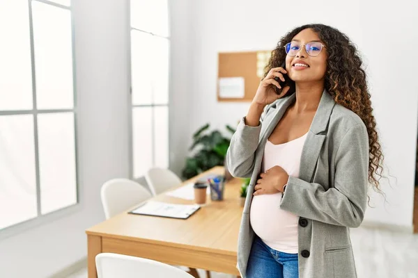 年轻的拉丁裔孕妇在办公室用智能手机自信地微笑交谈 — 图库照片