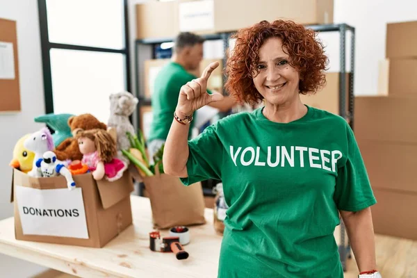 Bağışta gönüllü tişört giyen orta yaşlı bir kadın gülümseyen ve kendinden emin bir şekilde el hareketleriyle küçük beden işareti yaparak kameraya bakıyor. ölçüm kavramı. 