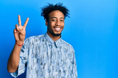 Sakallı, iki numaralı parmaklarıyla gösteriş yapan, kendinden emin ve mutlu gülümseyen Afro-Amerikalı genç adam.. 