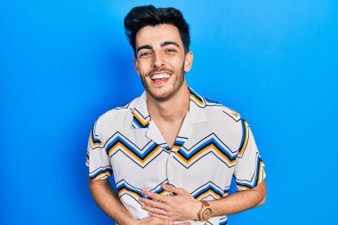 Gündelik kıyafetler giyen genç İspanyol adam gülümseyerek kahkahalarla gülüyor çünkü elleri vücutta olan komik, çılgın bir şaka.. 