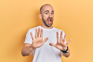 Sıradan beyaz tişört giyen genç kel adam korku ifadesinden korkmuş ve dehşete düşmüş. El hareketlerini durdur, şok içinde bağır. panik konsepti. 