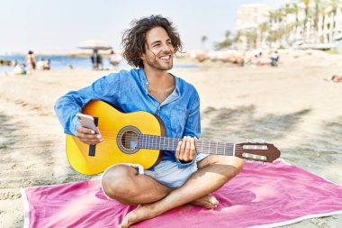 Genç İspanyol bir adam kumsalda oturmuş klasik gitar çalıyor..