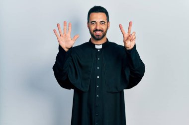 Sakallı, Katolik rahip cüppeli yakışıklı bir adam yedi numaralı parmaklarıyla kendini beğenmiş ve mutlu gülümserken kendini gösteriyor.. 