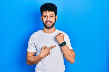 Sakallı, beyaz tişörtlü genç bir Arap. Saati, sabırsızlığı ve rahat bir ifadeyle kameraya bakması için acele ediyor. 