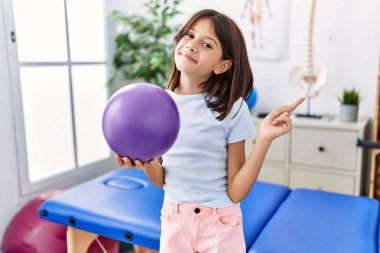 Küçük bir rehabilitasyon topu tutan genç İspanyol kız gülümsüyor. 