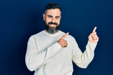Gündelik kıyafetler giyen genç İspanyol adam gülümseyip kameraya bakıyor ve iki eliyle ve parmaklarıyla kenarı işaret ediyor.. 