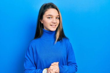 Balıkçı yaka kazak giyen genç esmer kız ellerini kavuşturup gülümsüyor ve rahatlıyor. Başarı ve iyimserlik 