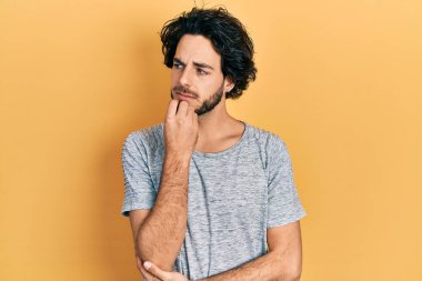 Yakışıklı, gri tişört giyen, kuşkuya odaklanmış, çenesinde parmak olan yakışıklı bir adam. 