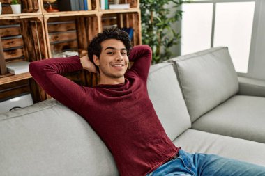 Elleri başının üstünde, evdeki kanepede oturan Latin asıllı genç adam..