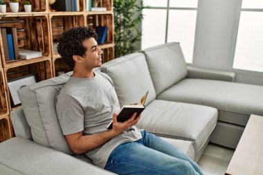 Evdeki kanepede oturmuş kitap okuyan genç bir İspanyol..