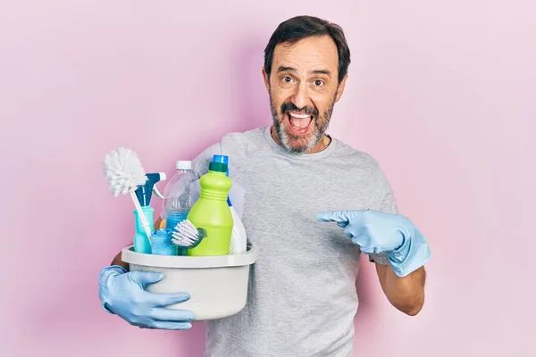 Middle age hispanic man holding cleaning products smiling happy pointing with hand and finger