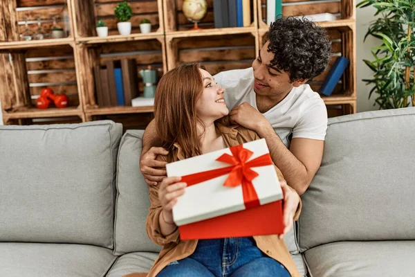 年轻夫妇坐在沙发上开心地笑着 带着结婚周年礼物在家里送礼 — 图库照片