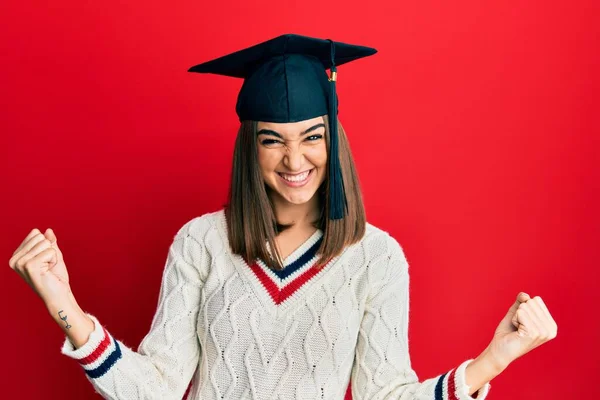 卒業キャップを身に着けている若いブルネットの女の子は非常に満足し 腕を上げて勝者のジェスチャーを行うことに興奮し 笑顔と成功のために叫んでいます お祝いのコンセプト — ストック写真
