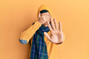 Yün şapka ve kış eşarbı takan yakışıklı İspanyol adam elleriyle gözlerini kapatıyor ve üzgün ve korku ifadeleriyle jest yapıyor. utangaç ve olumsuz kavram. 