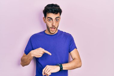 Gündelik tişört giyen genç İspanyol adam acele edip saati, sabırsızlığı ve gecikmeye kızmayı işaret ediyor. 