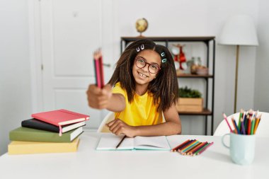 Evde elinde kalemlerle okul ödevi yapan Afrikalı Amerikalı bir kız.
