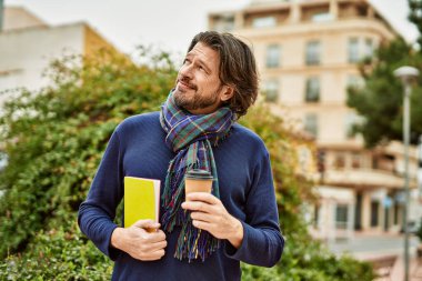 Orta yaşlı yakışıklı bir adam parkta bir fincan kahve içiyor.