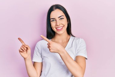 Mavi gözlü, sıradan beyaz tişörtlü, gülümseyen ve kameraya bakan iki eli ve parmakları yanda olan güzel bir kadın.. 