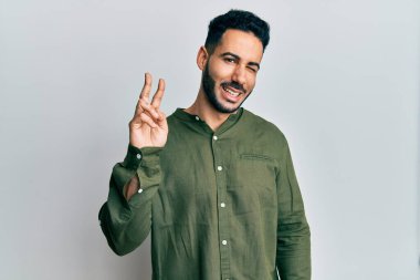 Gündelik kıyafetler giyen, gülümseyen ve kameraya göz kırpan genç İspanyol adam zafer işareti yapıyor. İki numara.. 