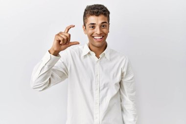 Genç, yakışıklı İspanyol bir adam izole edilmiş arka planda duruyor gülümsüyor ve kendinden emin bir şekilde el hareketi yapıyor parmaklarıyla işaret yapıyor ve kameraya bakıyor. ölçüm kavramı. 