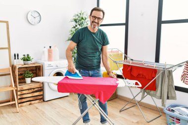 Orta yaşlı İspanyol adam evde giysileri ütülüyor..