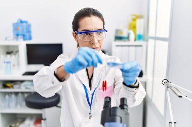 Laboratuvarda mikroskop kullanan genç İspanyol kadın bilim adamı üniforması giyiyor.