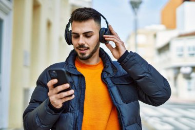 Yakışıklı, sakallı, neşeli, kendine güvenen, kışlık palto giyen, akıllı telefondan müzik dinleyen bir İspanyol.