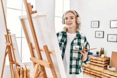 Sanat stüdyosunda resim yaparken ve müzik dinlerken gülümseyen genç sanatçı kız..
