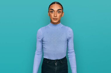 Makyaj yapan, uzun saçlı, sıradan kıyafetler giyen, ciddi ifadeli İspanyol transseksüel bir adam. Basit ve doğal bir şekilde kameraya bakıyorsun.. 